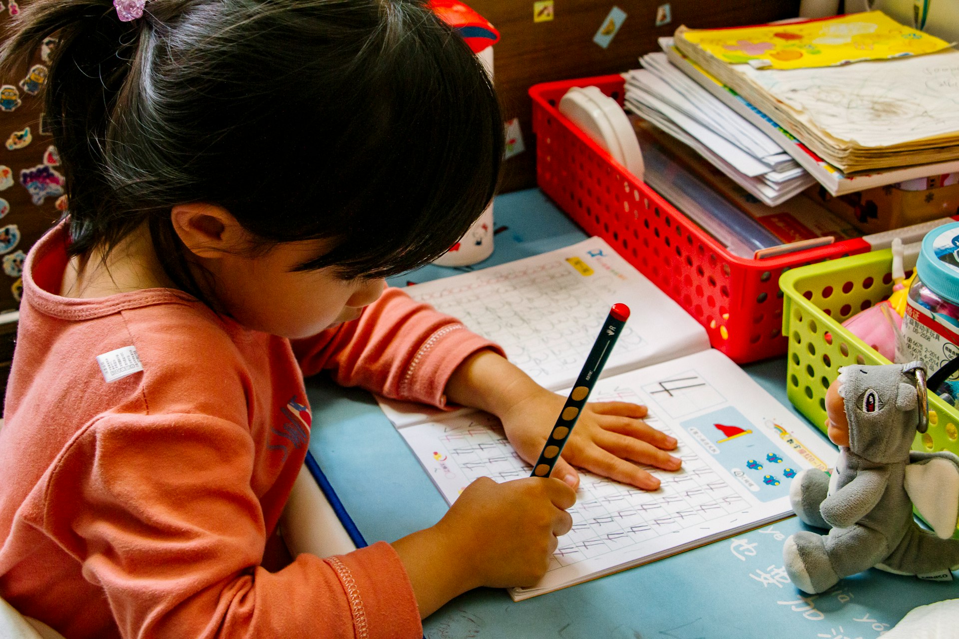 girl in orange long sleeve shirt writing on white paper